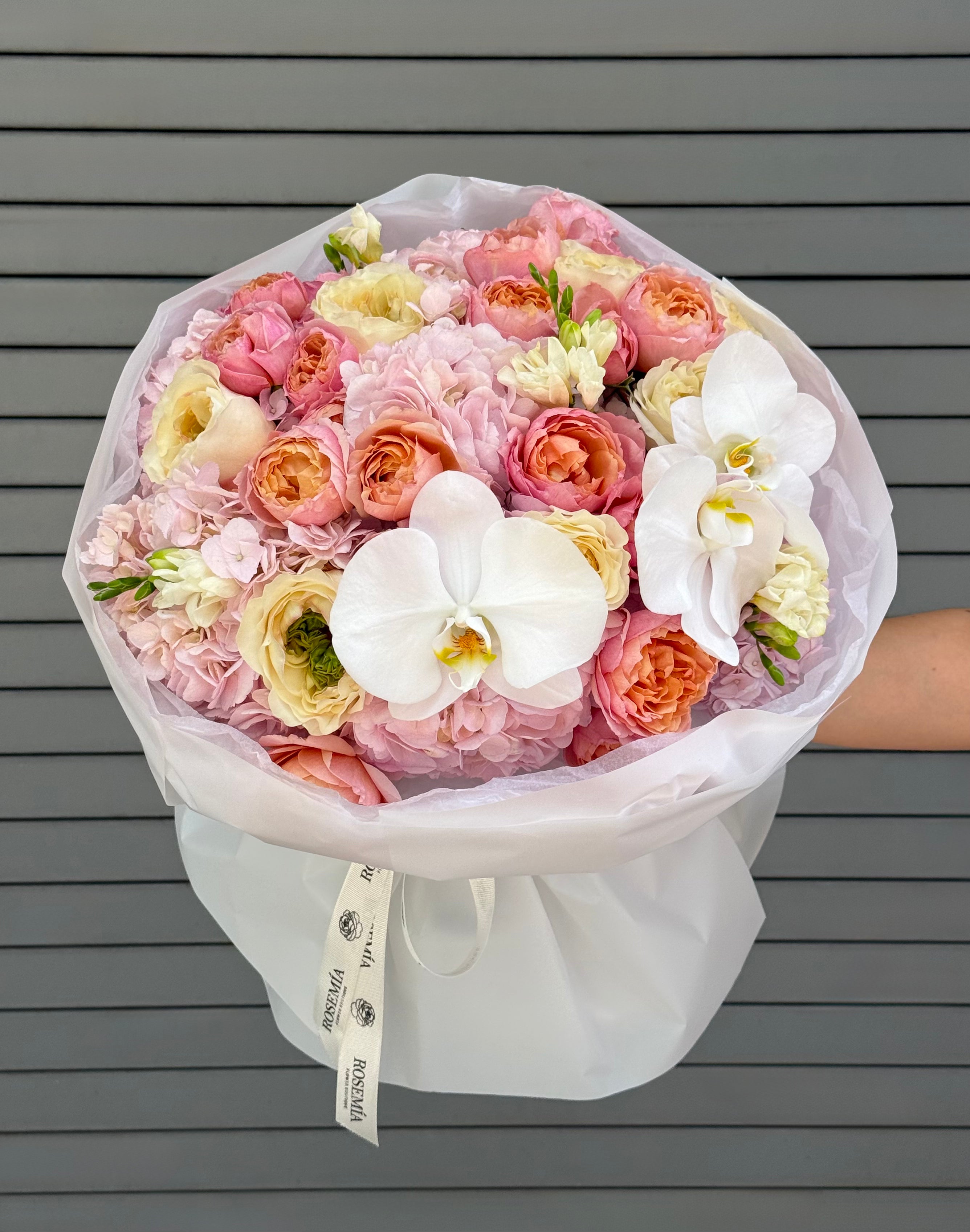 Bouquet of pink, white, and orange flowers with a white orchid held against a gray wooden background.
