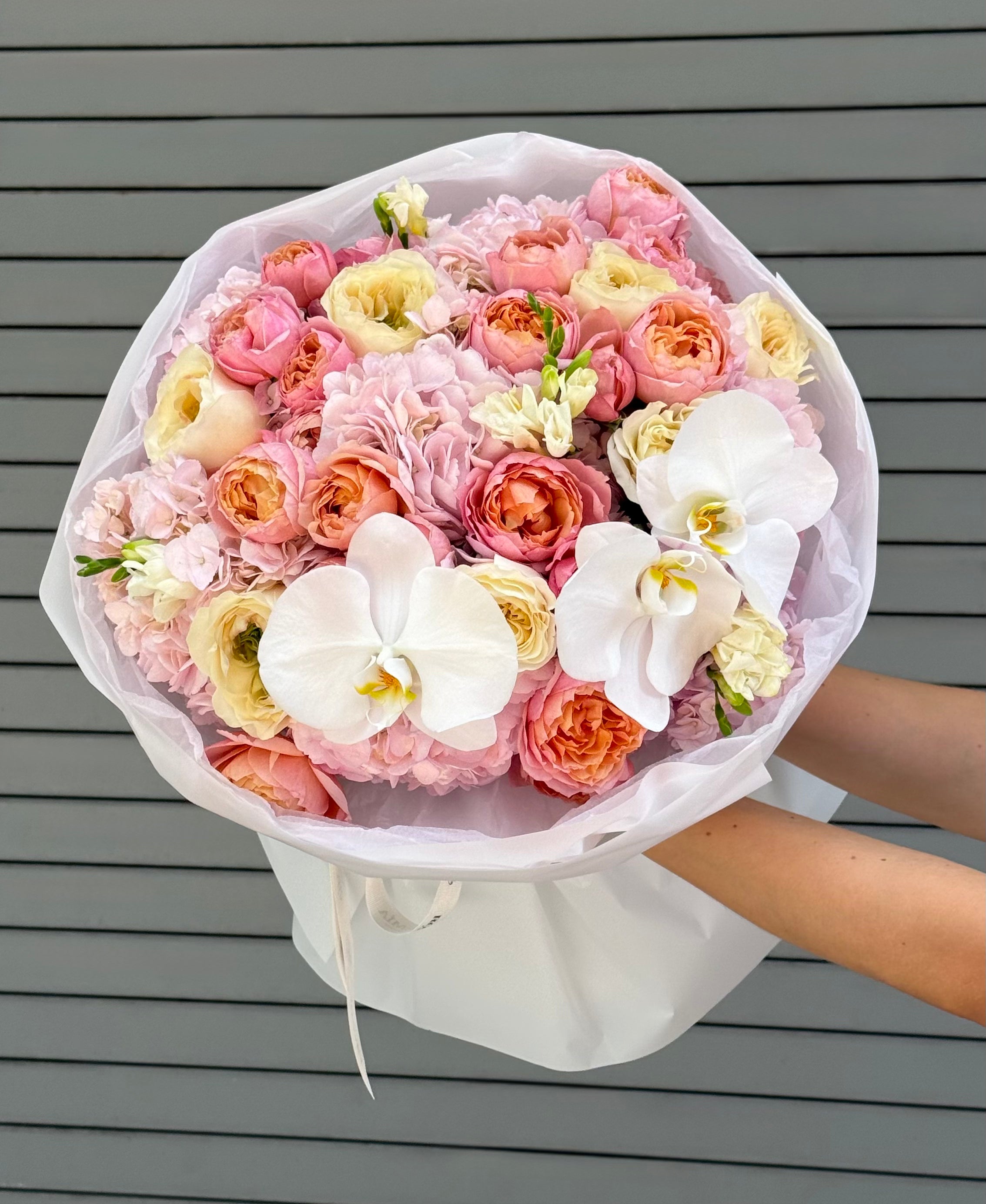 Bouquet of pink, white, and orange flowers held by a person against a gray wooden background