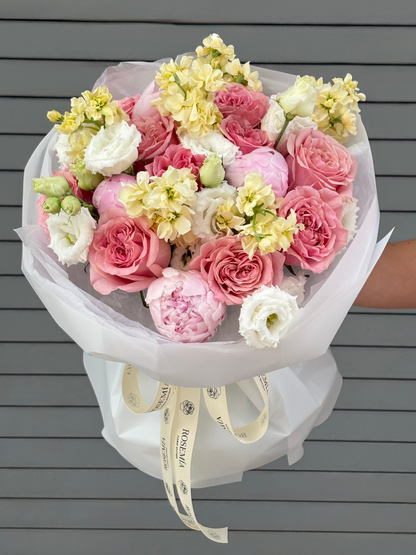 Bouquet of pink, white, and yellow flowers held against a gray wooden background